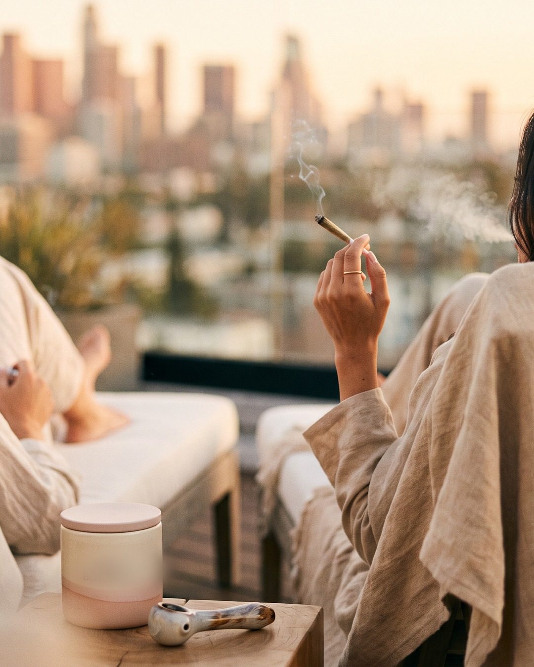 Two friends unwinding on a rooftop at golden hour, one holding a lit Gushy pre-roll