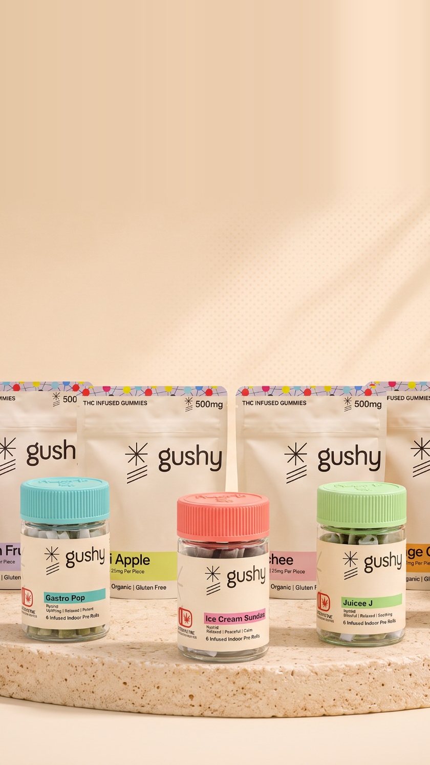 The Gushy line on a round travertine plinth: eight infused pre-roll jars in front of four live resin gummy pouches, with palm leaves in the corners