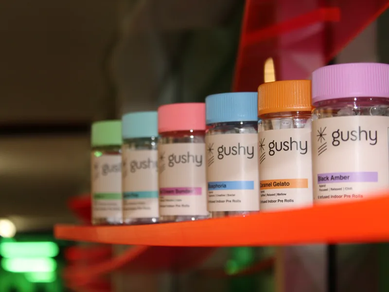 Six Gushy pre-roll jars lined up on an orange display shelf, lids forming a color run